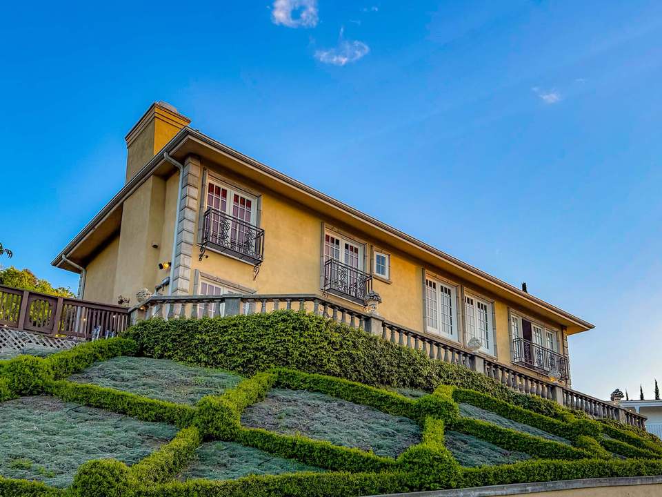 Spanish-style stucco house with wrought-iron Juliet balconies above a sculpted geometric front lawn