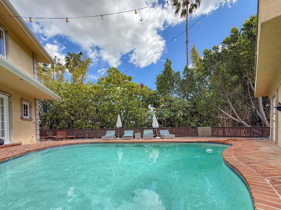 Oval saltwater pool on a terracotta brick deck with loungers, umbrellas and mature trees