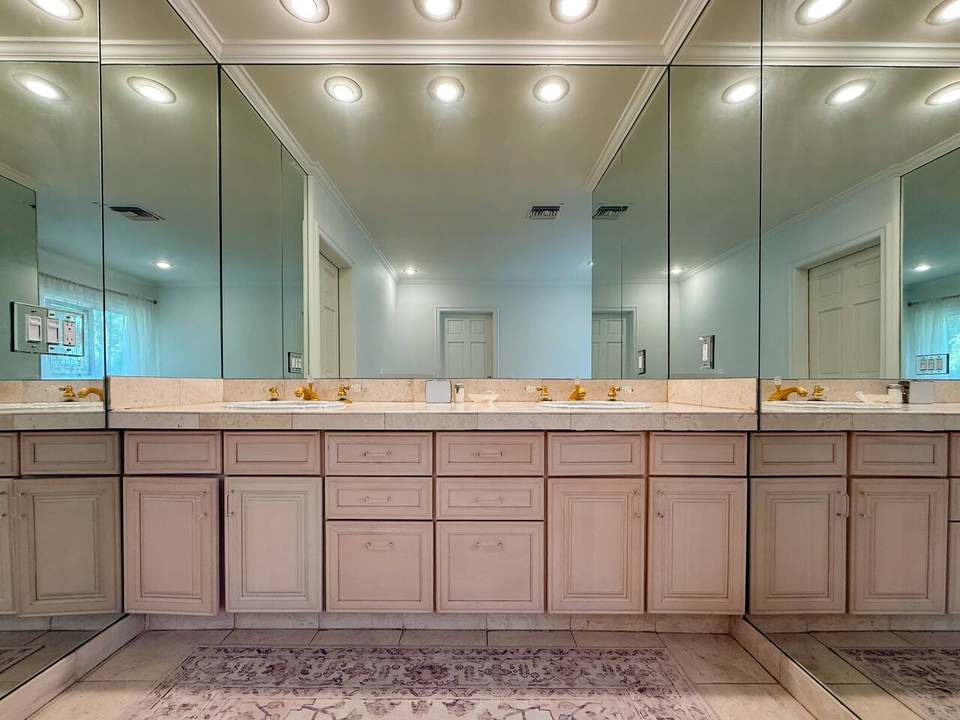 Primary bath double vanity with a wall-to-wall mirror and warm downlights